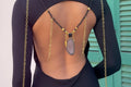 Person wearing a black swimsuit with gold and black beaded necklaces on a blurred background